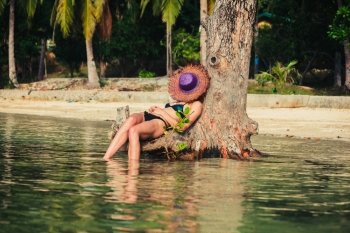 A sexy young woman wearing a bikini is relaxing by a tree on a tropical beach