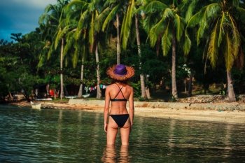 A young sexy woman wearing a bikini is standing in the water on a tropical beach