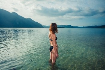 A young woman wearing a bikini is standing in the water and is looking at a tropical island