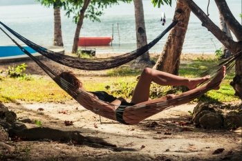 A young woman is relaxing in a hammock on a tropical beach in the shade