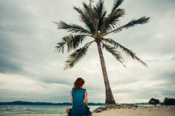 A young woman is sitting under a palm tree on a tropical beach