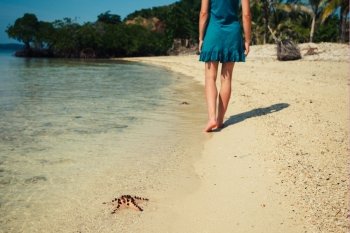A young woman is walking past a starfish on a tropical beach