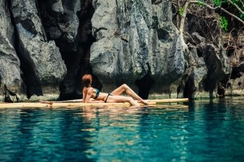 A beautiful young woman in a swimsuit is relaxing on a bamboo raft in a tropical lagoon