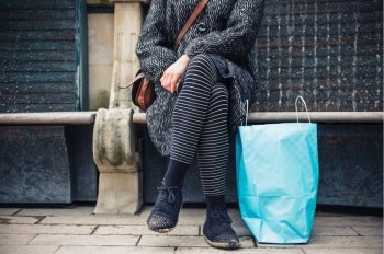 A young woman with a bag of shopping is resting on a bench in the city