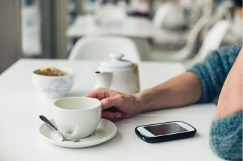 Closeup on the hands of a young woman as she is using her smartphone while having a cup of tea in a cafe
