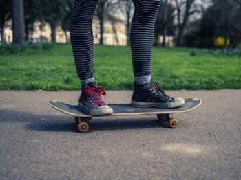 The legs of a trendy young person skteboarding on the concrete in a park