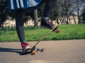 A young woman wearing trendy clothes is skateboarding in a park