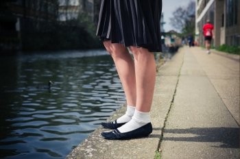 The legs of a young woman wearing a skirt as she is standing by a canal on a sunny day