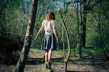 A young woman is walking amongst the trees and is exploring a mysterious forest