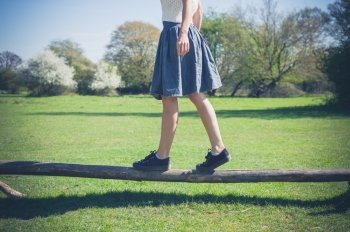 A young woman is walking in the forest and is balancing on a wooden beam