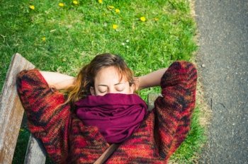 A young woman is sleeping on a bench in the park with a scarf covering her face