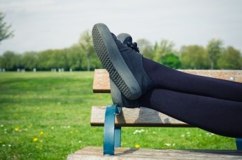 The legs of a young woman as she is lying on a bench in the park relaxing