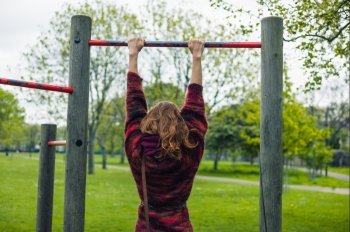 A young woman is doing pull ups in a park