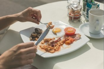 A young woman is having a traditional English breakfast at a table outside a cafe on the street