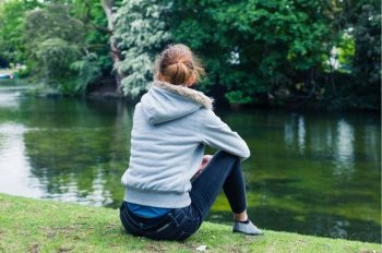 A trendy young woman is sitting by the water in a park