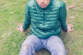 A trendy young man with a hole torn in his jeans at the knee is sitting on the grass