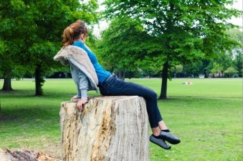 A trendy young woman is sitting on a tree trunk in the park