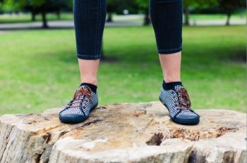 The feet of a trendy young woman standing on a tree trunk