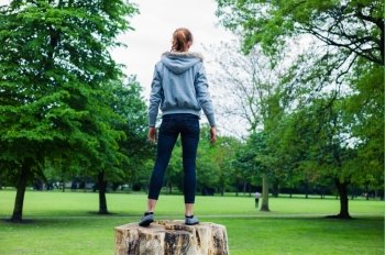 A young woman is standing on a tree trunk in a park
