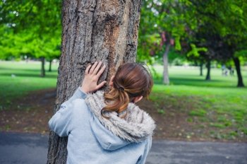 A young woman is hiding behind a tree in the park