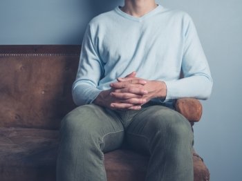 A young man is sitting on an old antique sofa with his hands folded