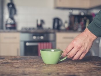 A male hand is placing a cup on a table in a kitchen