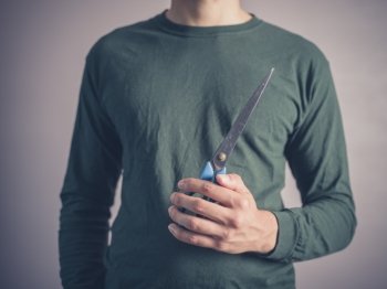 A young man wearing a green top is holding a pair of scissors