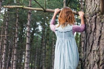 A young woman is climbing a tree in the forest