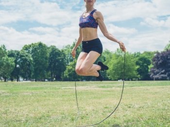 A fit and atheltic young woman is skipping on the grass in a park on a sunny summer day