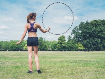 A fit and athletic young woman is twirling a hula hoop in the park on a sunny summer day