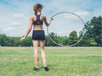 A fit and athletic young woman is twirling a hula hoop in the park on a sunny summer day