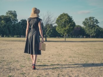 Vintage filtered shot of an elegant young woman in high heels and a dress walking in the park with a briefcase