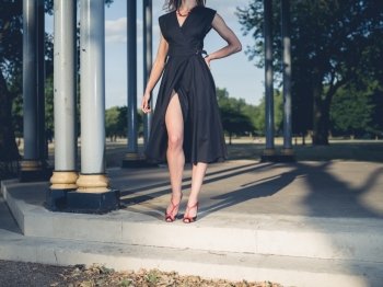 An elegant woman wearing a sexy dress is standing in a bandstand in a park at sunset