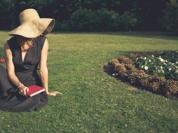 Vintage filtered shot of an elegant woman sitting on the grass in a park with a book