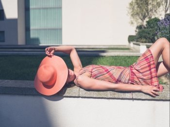 A young woman wearing a dress and a hat is relaxing outside on a sunny summer day