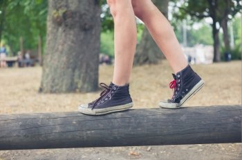 The feet of a young woman as she is walking on a wooden beam outside in the park