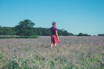 A young woman is standing in a field of purple flowers on a sunny summer day