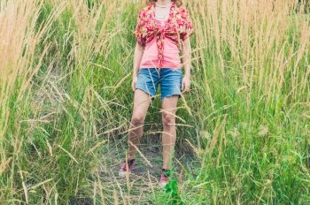 A young woman wearing shorts is standing outside in some tall grass