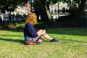A young woman is sitting on the grass in a park in the city on a sunny summer day