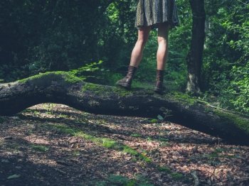 A young woman is standing on a log in a clearing in the forest