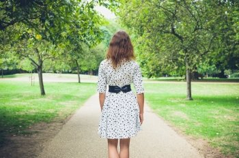 A young woman wearing a white dress is walking in the park