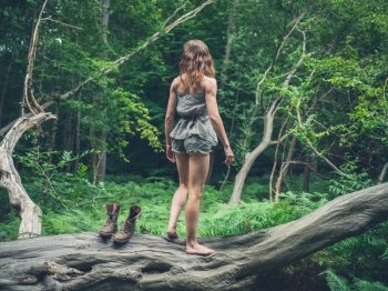 A young woman is standing barefoot on a fallen tree in the forest after having taken off her shoes