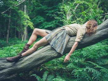 A young woman is lying on a fallen tree in the forest surrounded by ferns