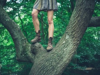 A young woman wearing a skirt is standing in a tree in the forest