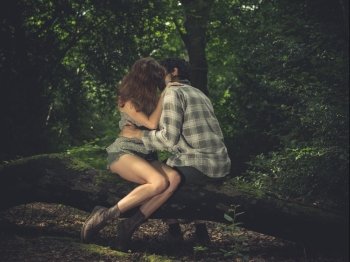 A young couple is sitting on a log in the forest and kissing