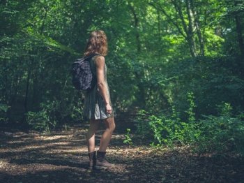 A young woman wearing a backpack is standing in a clearing in the forest