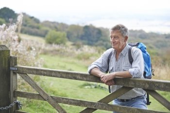 Senior Man Hiking In Countryside Resting By Gate