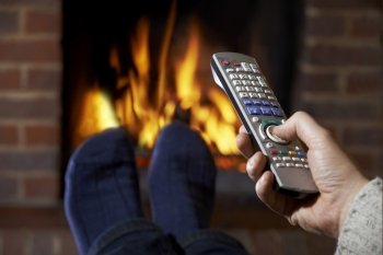 Man With Remote Control Watching Television And Relaxing By Fire
