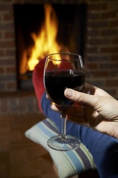 Woman With Glass Of Red Wine Relaxing By Fire
