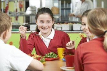 Group Of Pupils Sitting At Table In School Cafeteria Eating Lunch